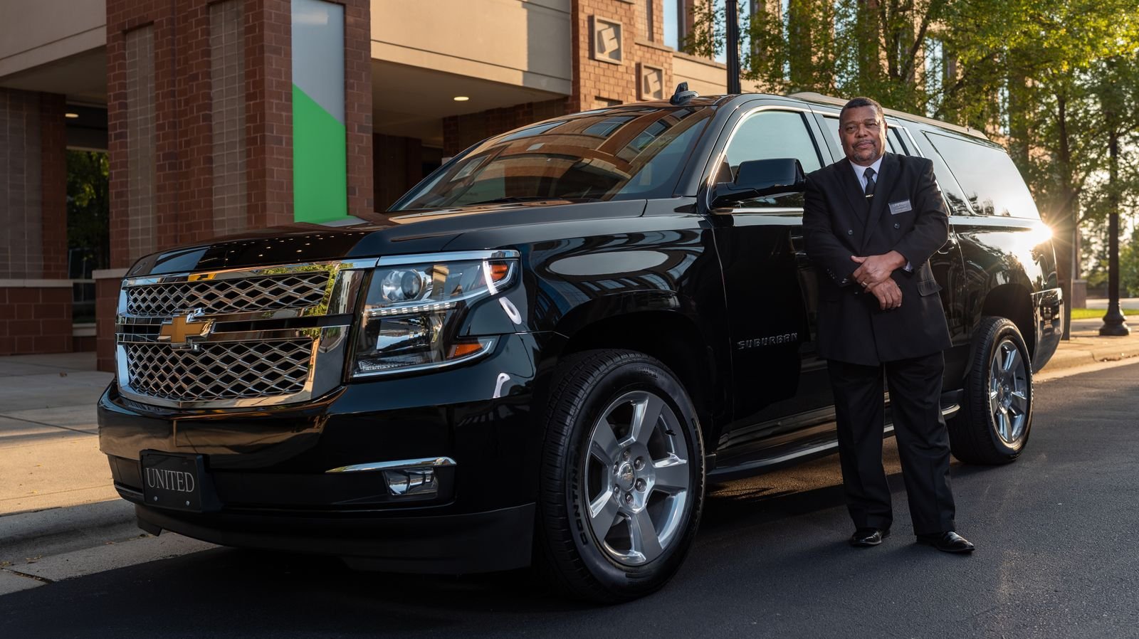 Chauffeur in a suit standing beside a black luxury SUV