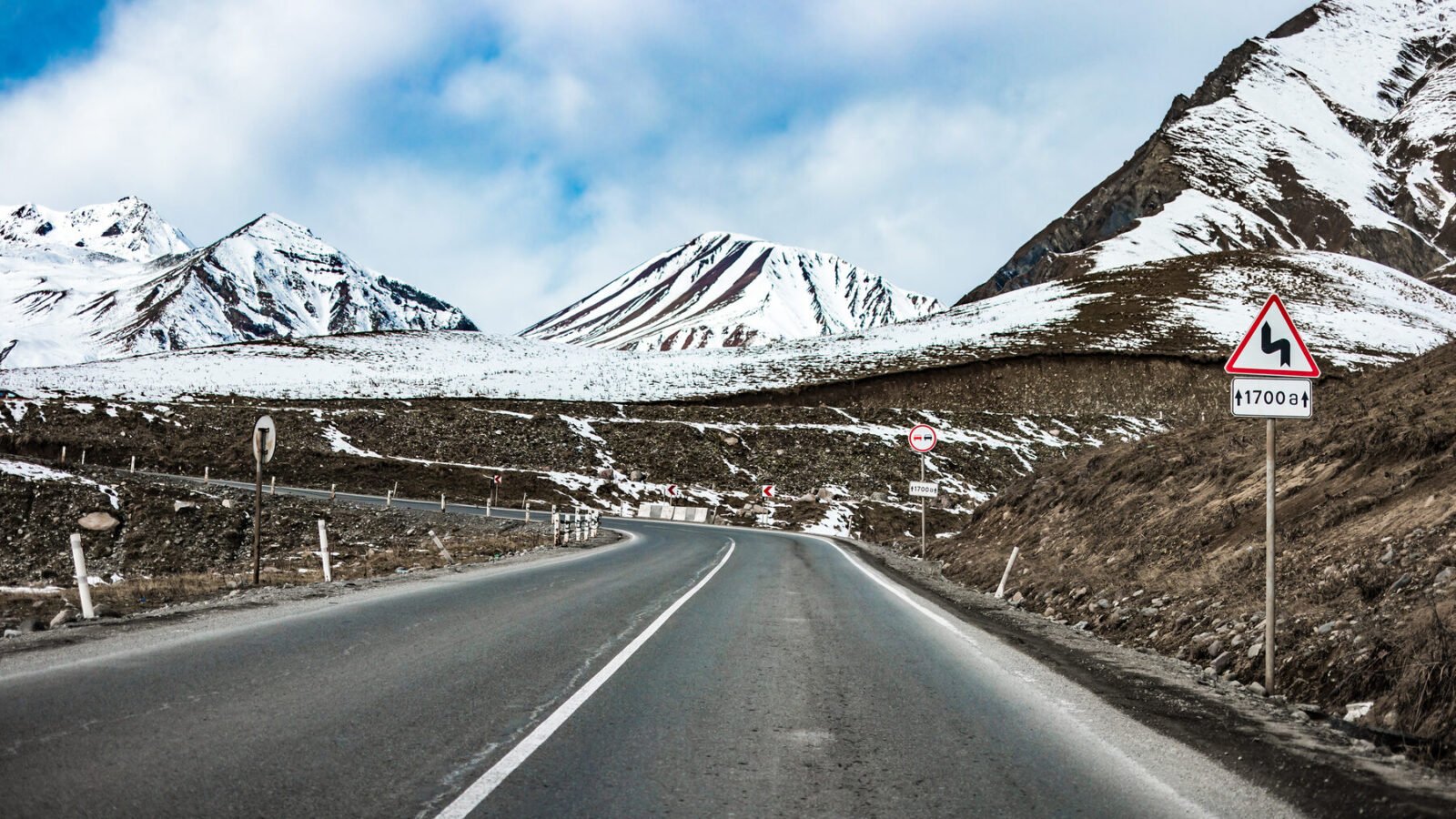 A mountain road in Georgia leading toward snow-capped Caucasus peaks
